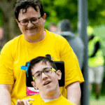 Dad with son using wheelchair, wearing matching t-shirts and community event