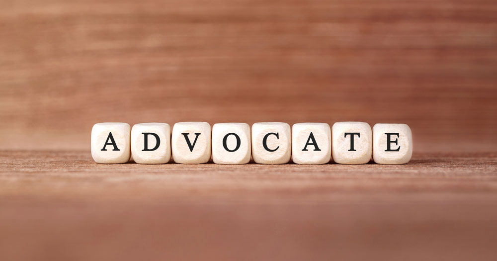 the word Advocate displayed in row of white tiles on wood grain background