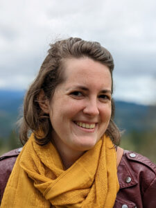 Jenn Buss in a maroon jacket and yellow scarf in front of an Oregon skyline