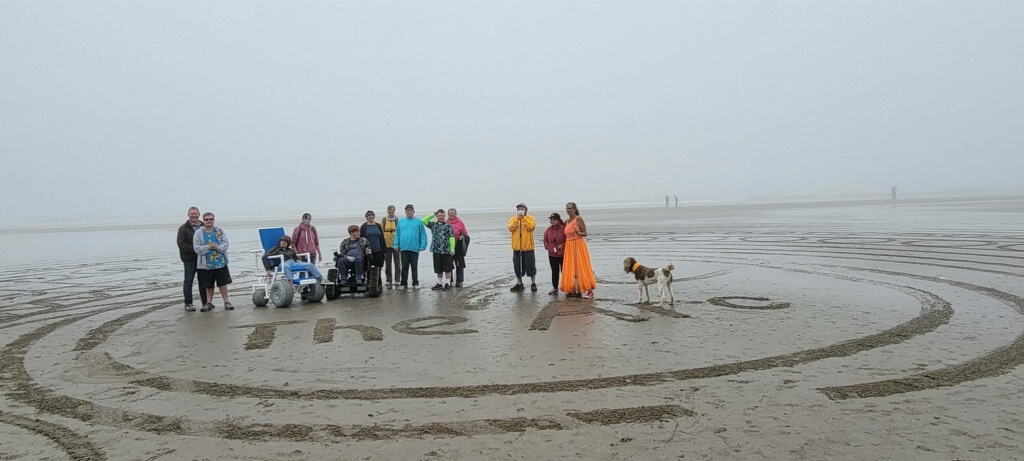 A group of people standing on the beach with "The Arc" written in the sand.