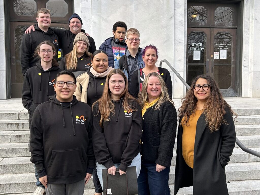 A group of people wearing black The Arc Oregon sweatshirts standing together on the steps of the Oregon State Capitol.